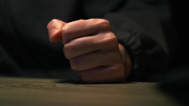 Aggressive behavior.
Aggressive hand gesture.
A clenched fist slamming on the table.
The man displays aggressive emotions.