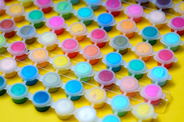 Colorful paint containers arranged on a yellow surface for art projects and creative activities in a studio setting