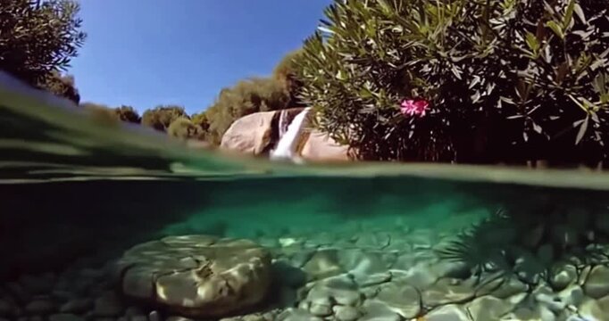 Waterfall Serenity: A unique split-level perspective showcases the clear, turquoise water of a tranquil stream, with a cascade of water gently flowing over rocks and into a vibrant, sunlit pool below.