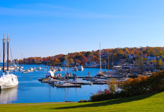 Panoramic daytime view of Camden Harbor in autumn with sailboats and fall foliage, classic coastal Maine New England maritime tourism concept