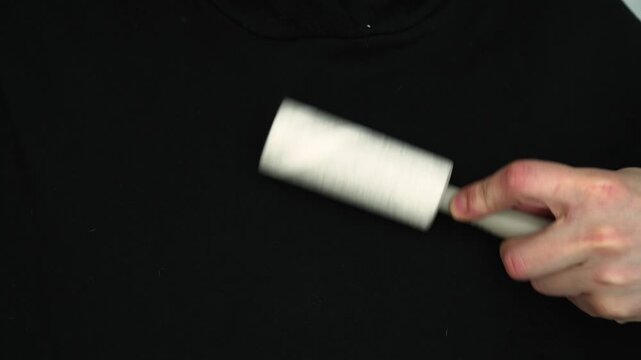 Cleaning lint from a sweater with a lint roller.
A person removes hair and dust from black clothing.