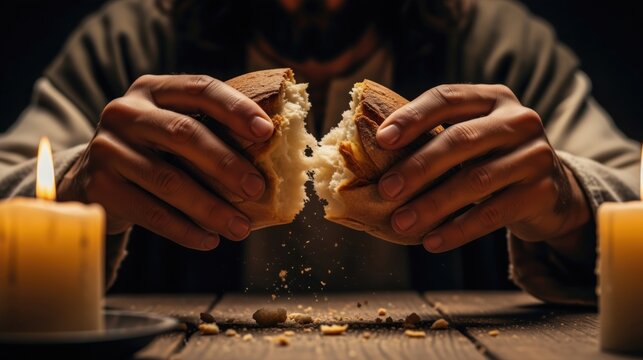 Close up of hands breaking a loaf of bread. Jesus Christ breaking bread at the Last Supper. Religious communion and Eucharist concept. Biblical scene with candlelight on a wooden table