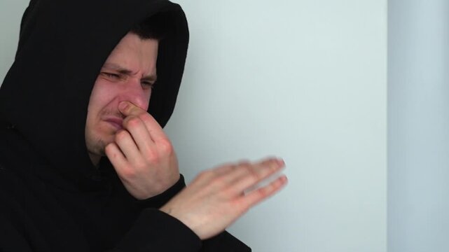 A man smells a foul odor and covers his nose.
The man is hiding from the stench in the room.
