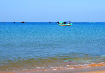 Obraz premium Fishing boat in sea on blue sky. View on ocean from beach. Fishing boats in sea along shore. Fishing Boat in lagoon in Vietnam.