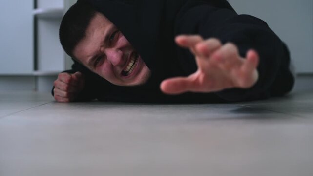 A man stretches his arm while lying on the floor.
The man falls to the floor and injures himself.
The man calls for help.