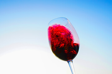 Red wine swirling on blue sky. Sommelier swirls with glass of red wine at sunset sky. Red Wine Swirling In Glass during vine Tasting, celebration vino party. Vibrant liquid splashing. Space for text