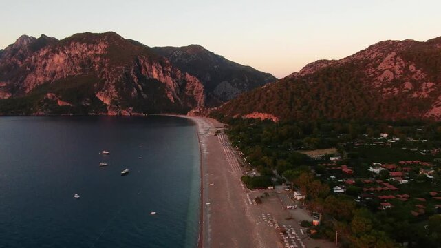 A breathtaking drone shot taken at sunrise on &Ccedil;ıralı Beach in Antalya. A panoramic view of the deep blue Mediterranean Sea, wide sandy beach, and the red reflection of the majestic Bey Mountains.