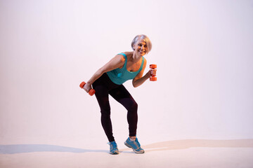 Fototapeta premium Active aging and healthy lifestyle concept: a fit middle-aged woman exercising with weights, smiling and looking motivated