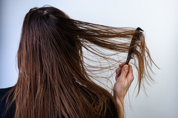 Young woman combing dirty oily hair on gray background.