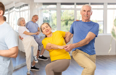 Obraz premium Enthusiastic senior couple, woman and man in sportswear, participating in group class for aged people, practicing energetic upbeat jive. Social dancing concept..
