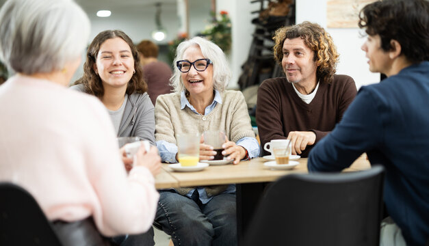 Family consisting of different generations sits at a large table in a cafe and discusses joint plans and holidays. Grandchildren communicate with their grandmothers in a coffee shop