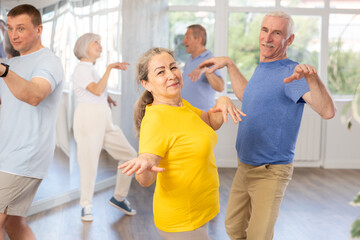 Obraz premium Smiling senior woman dancing vintage twist, popular in sixties, with characteristic arm movements paired with man in modern dance studio. Nostalgia for youth. Active hobbies concept..