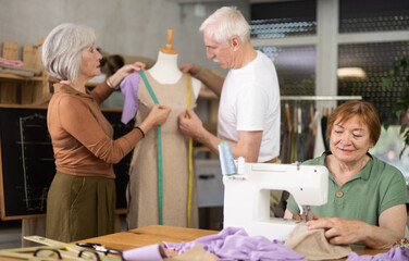 Obraz premium Group of elderly men and women sewing on machine and working with mannequin during master class
