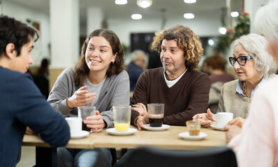 Fototapeta premium Joyful grandchildren chat with their grandmothers at a table in a coffee shop. Younger generation of the family communicates with the older generation with interest