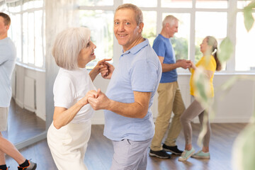 Fototapeta premium Happy smiling elderly man enjoying impassioned merengue with female partner in latin dance class. Social dancing concept..
