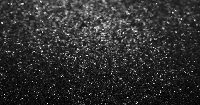 Dense field of tiny silver heart-shaped bokeh sparkles over a deep black background, fading into darker lower area. Elegant monochrome glitter texture for romance, luxury, and overlays.