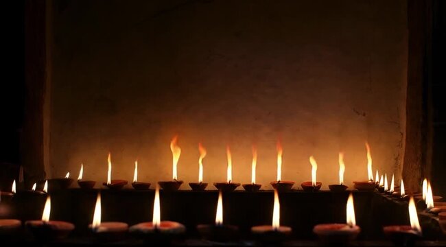 Rows of burning candles in dark interior, warm candlelight flame creating calm spiritual and memorial atmosphere