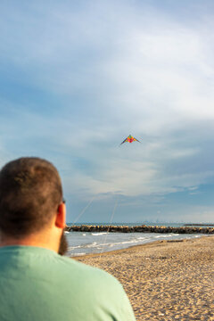 cabeza de hombre de espaldas volando una cometa de colores de dos manos en la playa