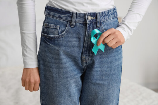 Young woman holding turquoise ribbon in bedroom. Cervical Health Awareness Month