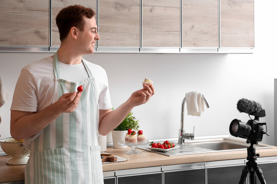 Young man with sweet muffins and fresh strawberries recording cooking video in kitchen