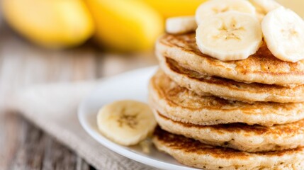 A stack of pancakes sits on a white plate with banana slices on top