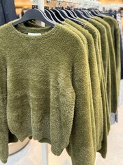 Row of green knit sweaters hanging on clothing rack in a retail store, cozy textured apparel display showing autumn or winter fashion collection.