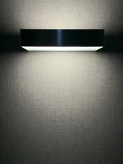 Modern wall mounted light fixture illuminating a textured wall, minimalist interior lighting creating a soft glow and clean contemporary design atmosphere.