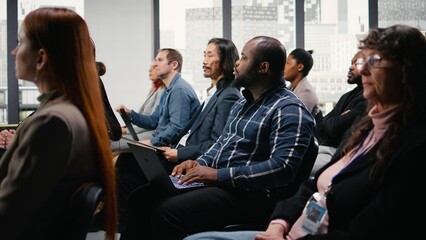 Black businessman takes notes on laptop at professional summit, forum conference with panel...