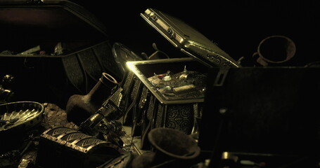 A collection of ornate treasure chests stands open, spilling out gold coins and ancient artifacts in a dark and mysterious setting. Shadows play across the treasure, highlighting its value. © icetray