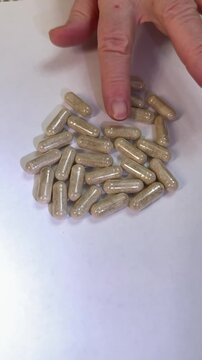 Caucasian woman sorting supplement capsules on white surface, closeup hand selecting herbal tablets from scattered pile, slow methodical motion, careful dosage planning, soft studio