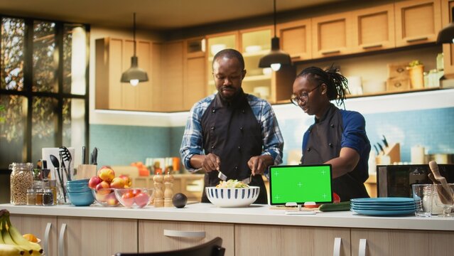 Isolated mockup tablet next to people doing meal prep in the kitchen, man and woman cooking and spending time together at home. Happiness and healthy lifestyle, bonding with joy.