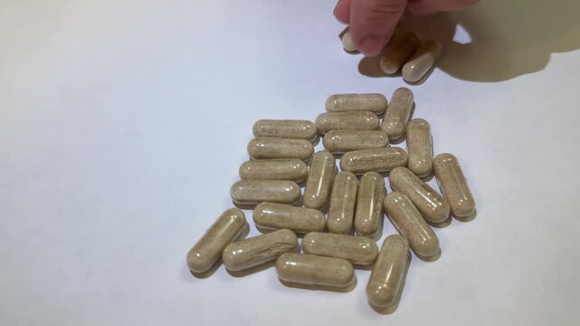 Caucasian woman sorting supplement capsules on white surface, closeup hand selecting herbal tablets from scattered pile, slow methodical motion, careful dosage planning, soft studio