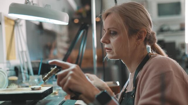 Focused female jeweler soldering jewelry with torch