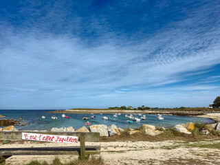 Calm coastal landscape with boats in the water and rocks on the shore under a clear blue sky.