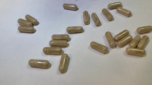 Caucasian woman sorting supplement capsules on white surface, closeup hand selecting herbal tablets from scattered pile, slow methodical motion, careful dosage planning, soft studio