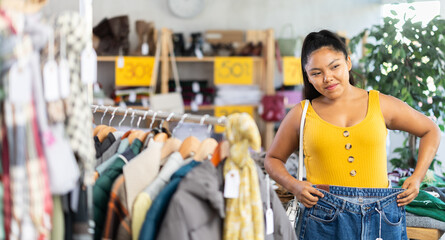 Fototapeta premium Positive young woman chooses fashionable jeans in a clothing store