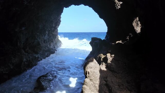 Wild ocean waves dramatically crashing against the dark volcanic rocks inside a sea cave, revealing a stunning view of the blue water and clear sky at Charco del Palo in Lanzarote