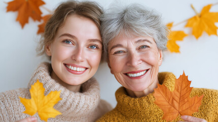 Happy intergenerational pair in autumn sweaters holding maple leaves