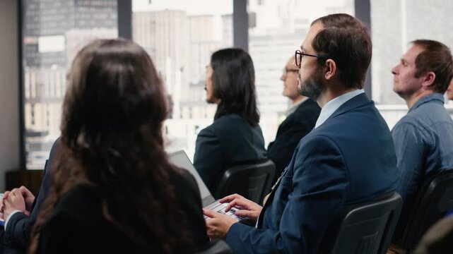 Business consultant takes notes on laptop during international conference event, speaker takes the stage for a presentation. Audience of professionals and participants engage in discussion. Camera B.