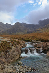 Fairy Pools waterfall on Isle of Skye, Scotland; cascading stream through rocky Scottish Highland landscape with dramatic mountains and colourful autumn fall vegetation under moody sky