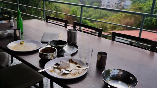 Outdoor restaurant table after meal with empty plates cups and utensils on a wooden table, showing casual dining atmosphere, finished lunch scene, leftover food traces, and relaxed mood of shared eati