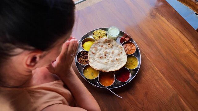 Overhead view of a woman in peach dress sitting at a wooden table with hands raised in excitement before eating Indian thali meal, showcasing cultural appreciation, joy of traditional Indian food, and