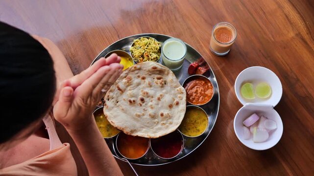 Overhead view of a woman in peach dress sitting at a wooden table with hands raised in excitement before eating Indian thali meal, showcasing cultural appreciation, joy of traditional Indian food, and