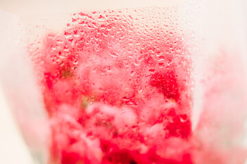 Close view of water droplets on a glass containing red liquid with red objects inside