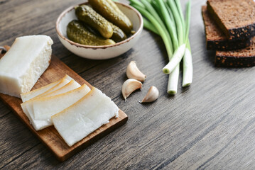 Pork fatback on a wooden cutting board with slices of rye bread, garlic,