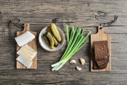 Pork fatback on a wooden cutting board with slices of rye bread, garlic,