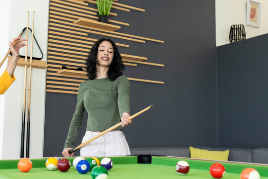Friends playing at pool table with green felt, adult female in olive top holding wooden cue