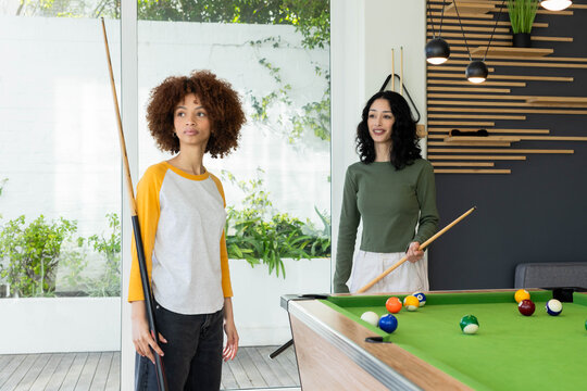 Diverse female friends playing pool in modern recreation room with green felt table cues