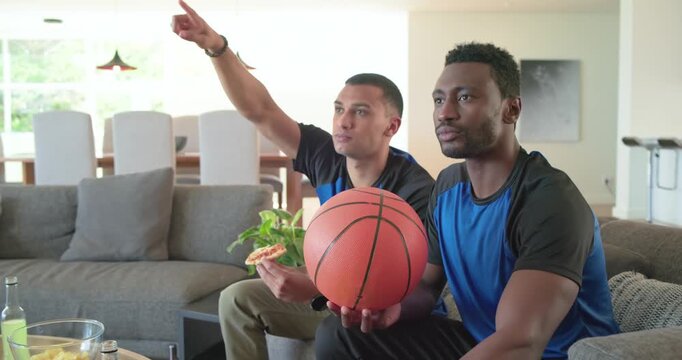 Diverse male friends watching sports broadcast rotating basketball and nibbling pizza at home