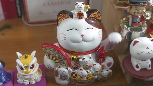 Close-up video showcases ceramic maneki-neko figurines.  The first shot focuses on a large cat.  The middle shows multiple figures.  The final view highlights a smaller cat